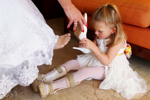 Laura, the brides daughter and flower-girl with leg braces helps her mother put on bride shoes at a wedding