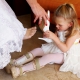 Laura, the brides daughter and flower-girl with leg braces helps her mother put on bride shoes at a wedding