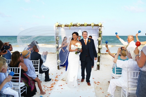 Guests shake maracas as bride and groom exit beach wedding at belmond maroma resort