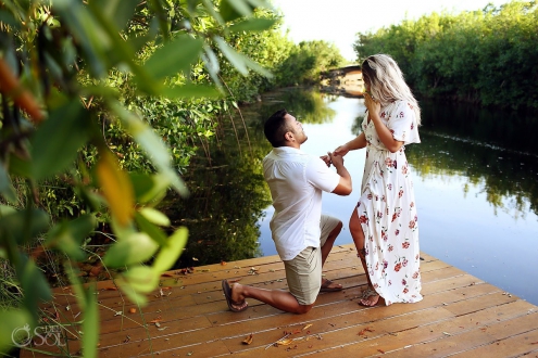 Kneeling down groom to be asks the question surprise proposal at the pier Andaz Mayakoba resort Riviera Maya engagement photographer del Sol Photographer