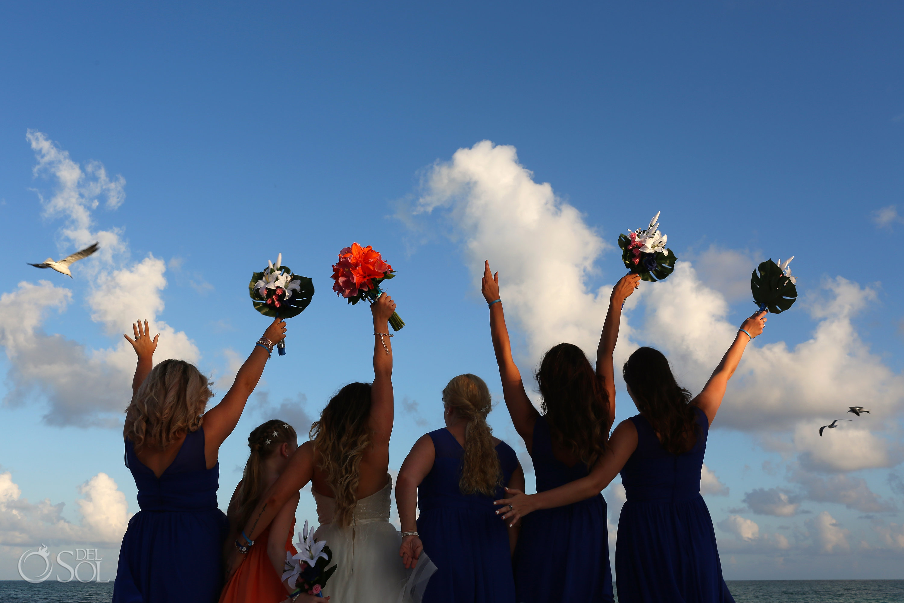 Wedding party photo ideas bride and bridesmaids with hands in the air with birs flying overhead Iberostar Paraiso del Mar Wedding