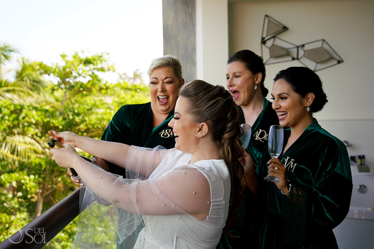 bride and bridesmaid opening champagne wearing custom green velvet robes