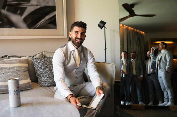 groom getting ready at Secrets Moxche wearing cream tie beige vest with groomsmen drinking beer