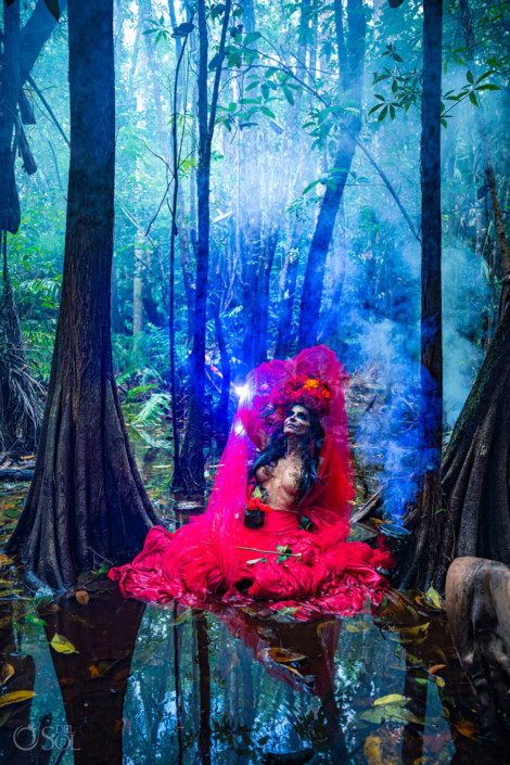 Catrina de la Rosa wearing red in the jungle sitting in the water with smoke Festival de día de muertos La Catrina Fest CDMX