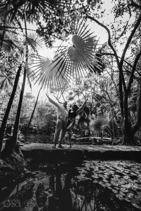 black and white photograph of a couple standing under huge palm leaves beside waterlilies