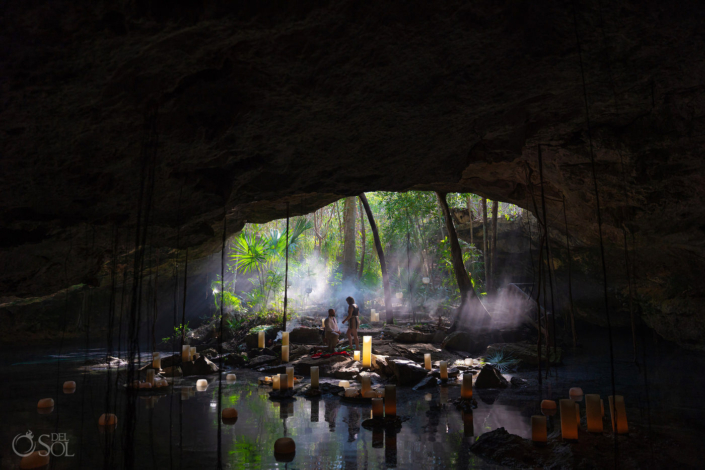 couple silhouetted in the best location for an epic proposal in Tulum Mexico is this stunning natural cenote cave with water reflecting the candles and light