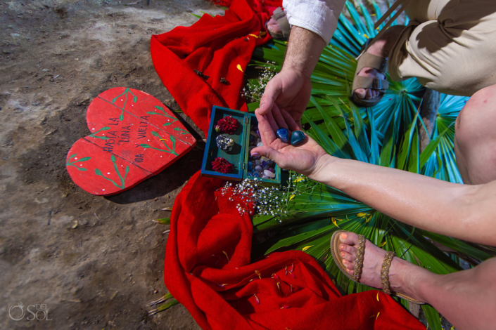 hands holding semi precious stones in front of a painted wooden sign that reads: to the moon and back in Spanish