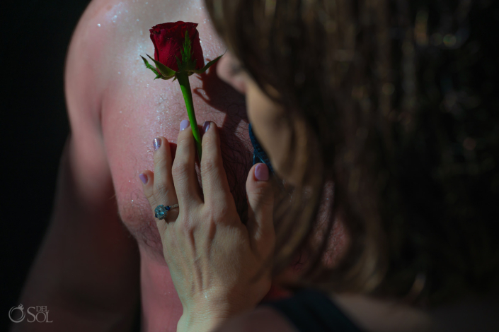 bride-to-be's hand holding a red rose wearing an engagement ring on her fiance's chest