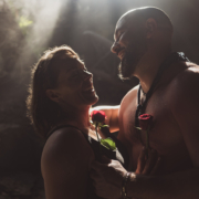 bare chested groom to be shows off his muscles in romantic engagement photo holding his newly engaged fiancee and 2 red roses