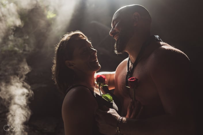 bare chested groom to be shows off his muscles in romantic engagement photo holding his newly engaged fiancee and 2 red roses