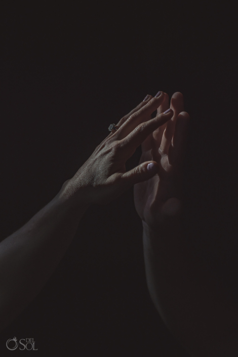 dark and moody editorial style engagement photograph of couple touching fingertips showing off diamond engagement ring