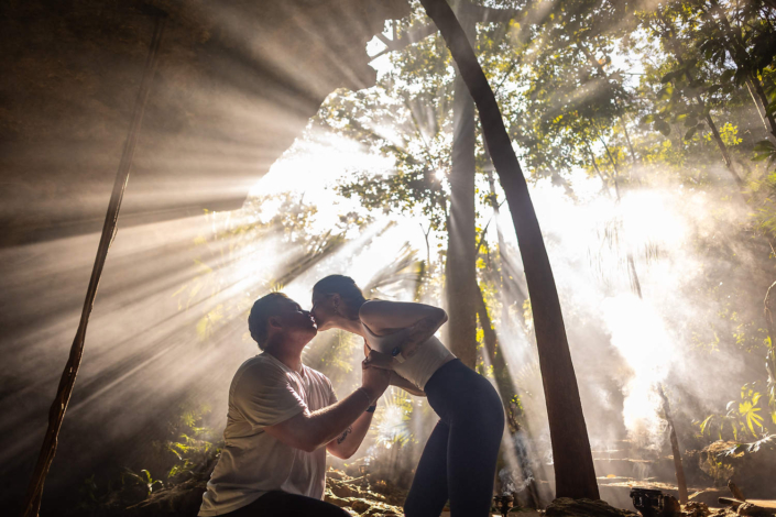 Intimate lighting, epic beams, inside a Luxury cenote engagement photography session, in the Riviera Maya with dramatic rock formations and tropical atmosphere
