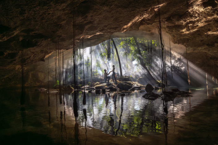 Professional cenote engagement photos in the Riviera Maya featuring a couple surrounded by turquoise water, limestone walls, and natural jungle light