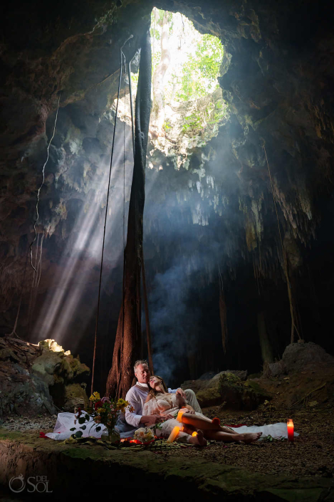 Couple standing beneath a beam of light inside a hidden cenote cave