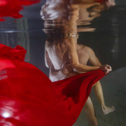 Artistic underwater cenote couple session featuring flowing red fabric and intimate connection inside a cave inspired by Adam and Eve