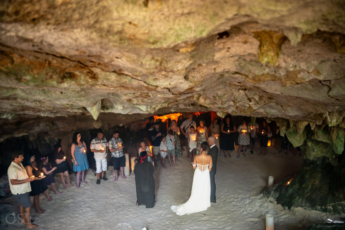 Guests witnessing an intimate family wedding ceremony inside a candlelit cenote.