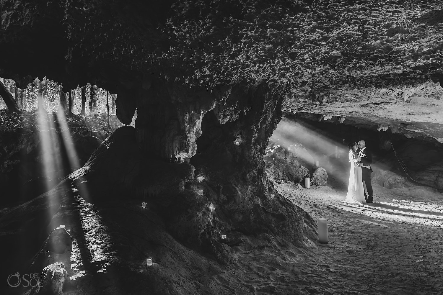 Bride and groom kissing beneath golden rays of sunlight inside a cenote.