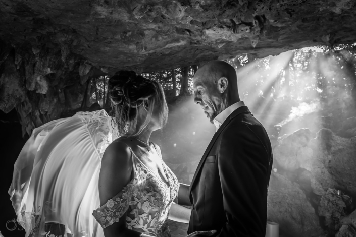 black and white portrait Bride and groom standing together in copal smoke with light beams inside the cave.