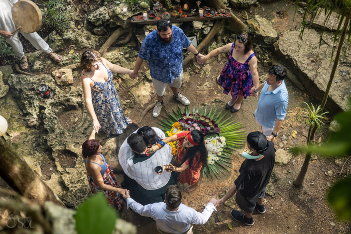Cenote ceremony with guests holding hand for a couple blessing with flower altar