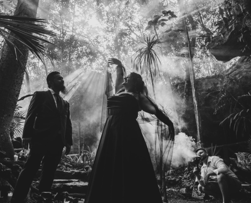 Bride in a black wedding dress beneath jungle light.